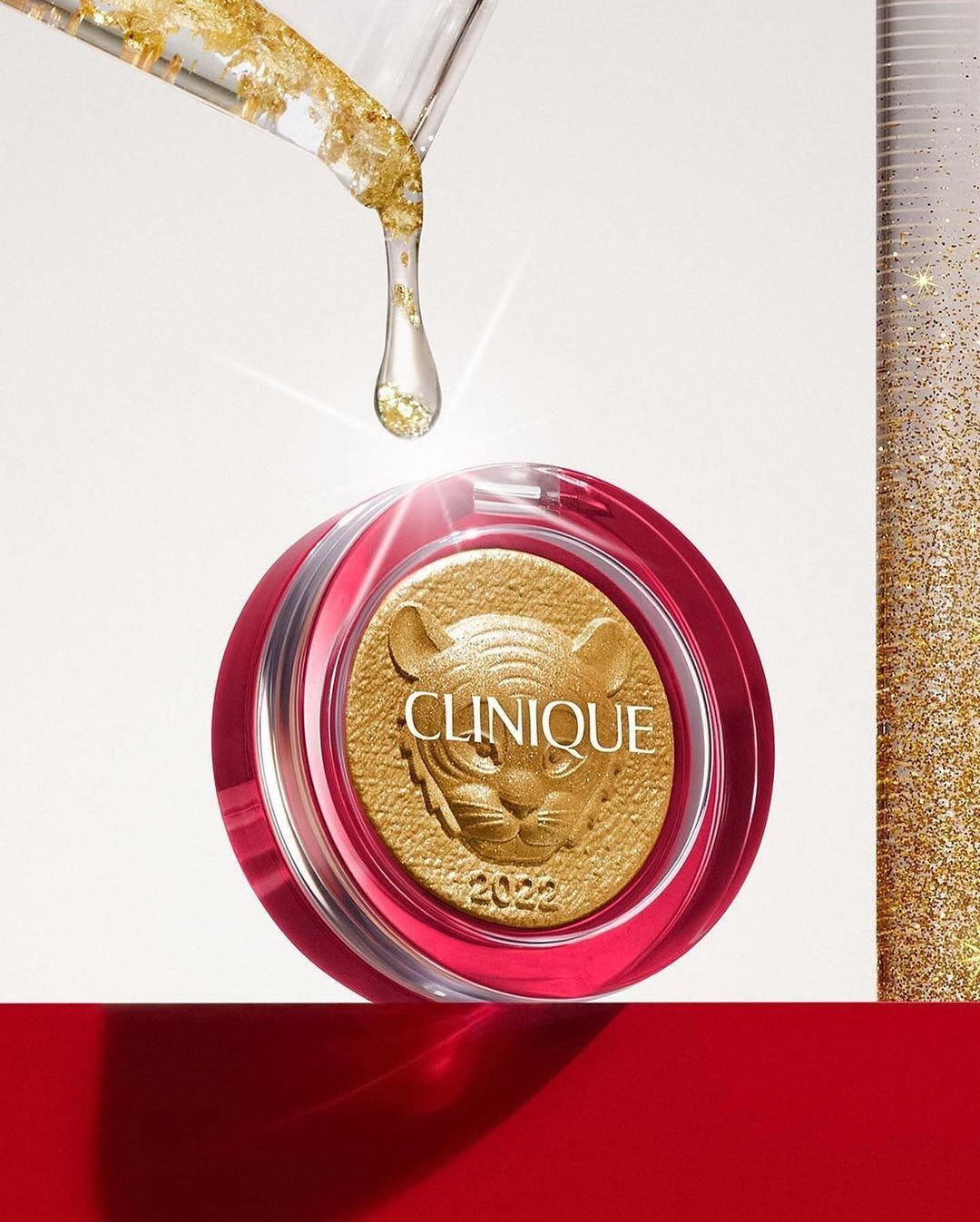 Close-up of Clinique product with golden tiger design, clear dropper with gold flakes, against a bright background with red platform.