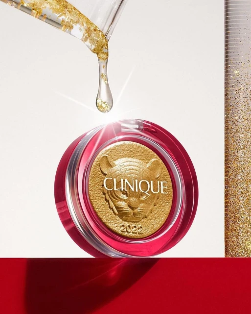 Close-up of Clinique product with golden tiger design, clear dropper with gold flakes, against a bright background with red platform.