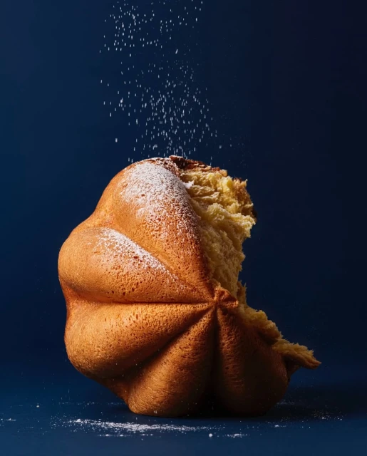 Close-up of a domed brioche pastry, sprinkled with powdered sugar, against a dark blue background, in a studio food photography setup.