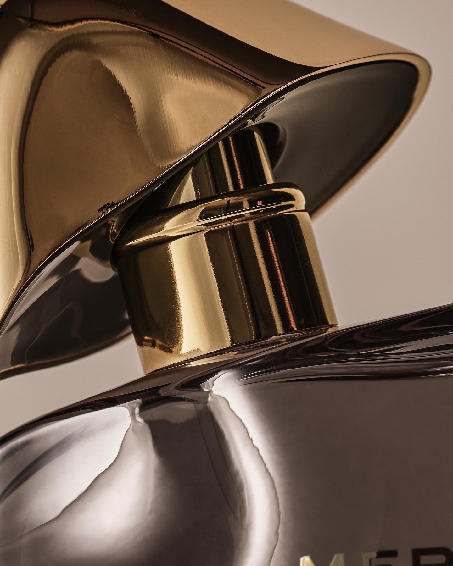 Close-up of a gold and silver reflective perfume bottle with a sculptural top, showcasing luxury and abstract design elements.