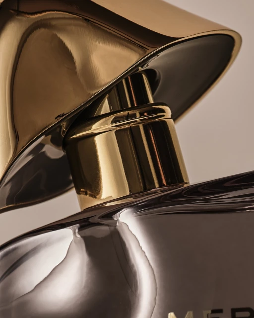 Close-up of a gold and silver reflective perfume bottle with a sculptural top, showcasing luxury and abstract design elements.
