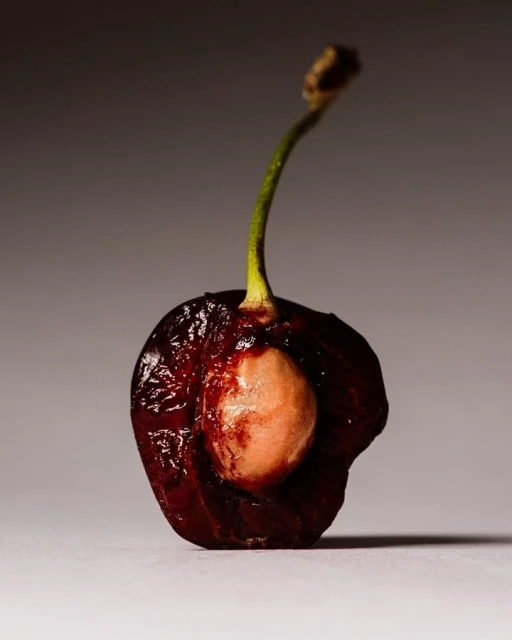 A detailed close-up of a halved dark cherry reveals its smooth pit. The fruit's stem is still attached, set against a gradient backdrop.