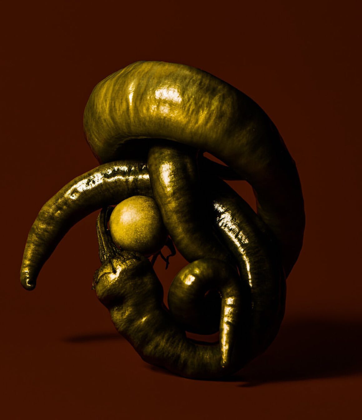 Abstract still life featuring twisted green chili peppers and a single yellow lemon in a close-up studio shot with a dark brown background.