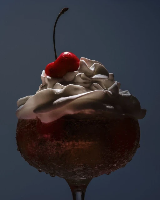 Close-up studio shot of a stemmed glass filled with a tan-colored liquid topped with whipped cream and a bright red cherry.