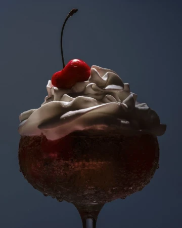Close-up studio shot of a stemmed glass filled with a tan-colored liquid topped with whipped cream and a bright red cherry.