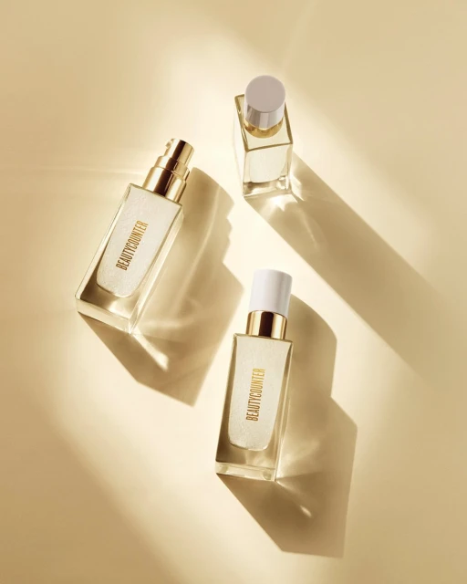 Three Beautycounter glass bottles are displayed on a light tan surface with soft shadows in a cosmetic product shot.