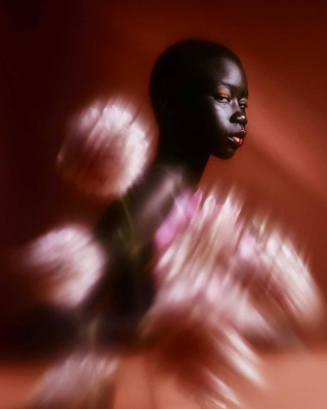 Portrait of an African American woman with dark skin and red lipstick, posing in front of a red background with light and pink floral elements.