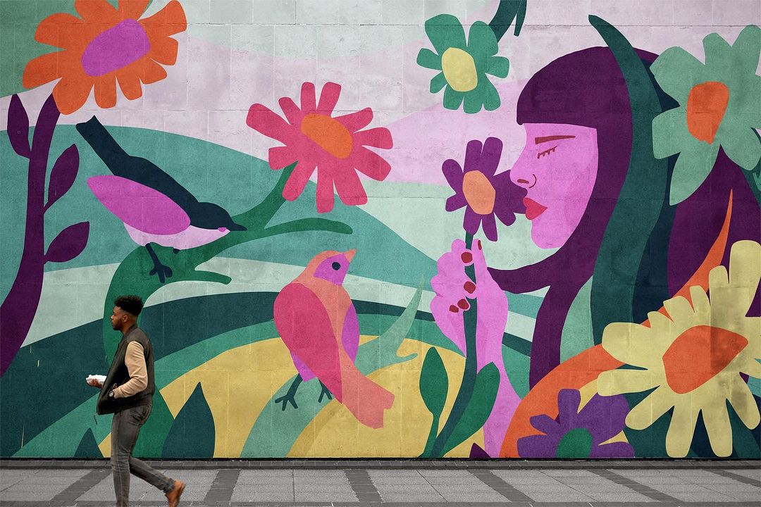 Man walks by a mural featuring an illustration of a woman with flowers and birds in a colorful, cartoon-like style on a city street.