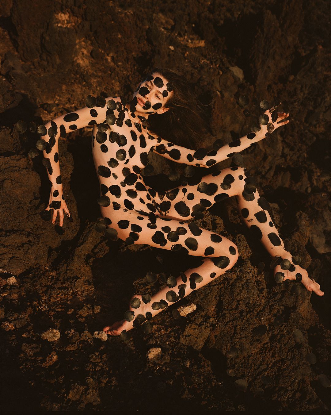 Artistic nude woman with body paint poses on a textured brown background, creating an abstract and visually striking composition.