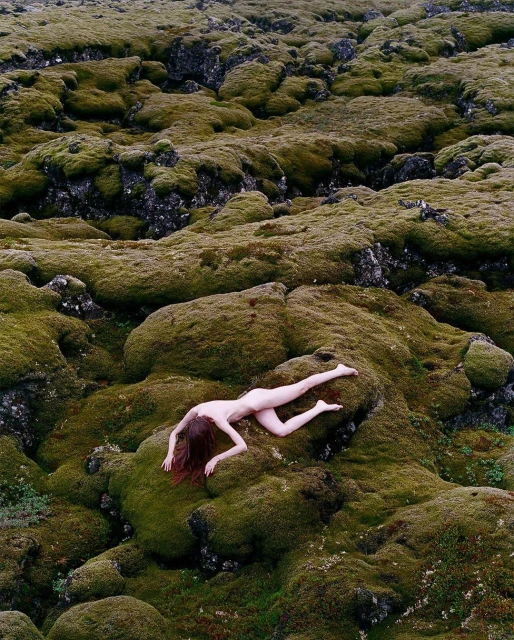 Woman lying down in a mossy landscape. Ground is covered with green moss and small rocks. The photo has an artistic and serene feel.