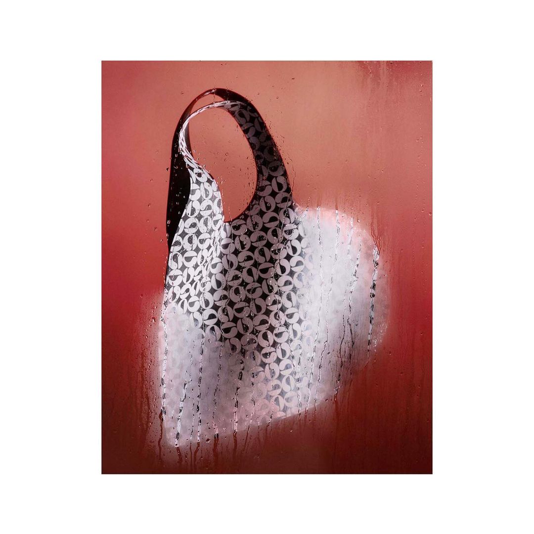White tote bag with a circular pattern against a diffused pink background with water droplets, creating an ethereal and artistic image.