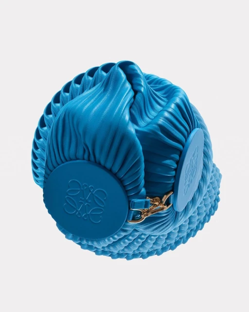 Close-up studio shot of a blue Loewe bag with a circular disc featuring the brand logo, showcasing its unique pleated design and textures.