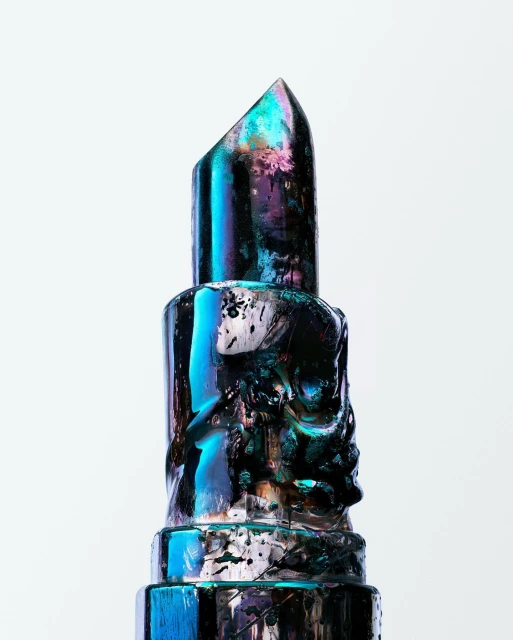 Close-up of sculptural lipstick, showcasing iridescent blue and purple hues and unique textured carvings against a white background.