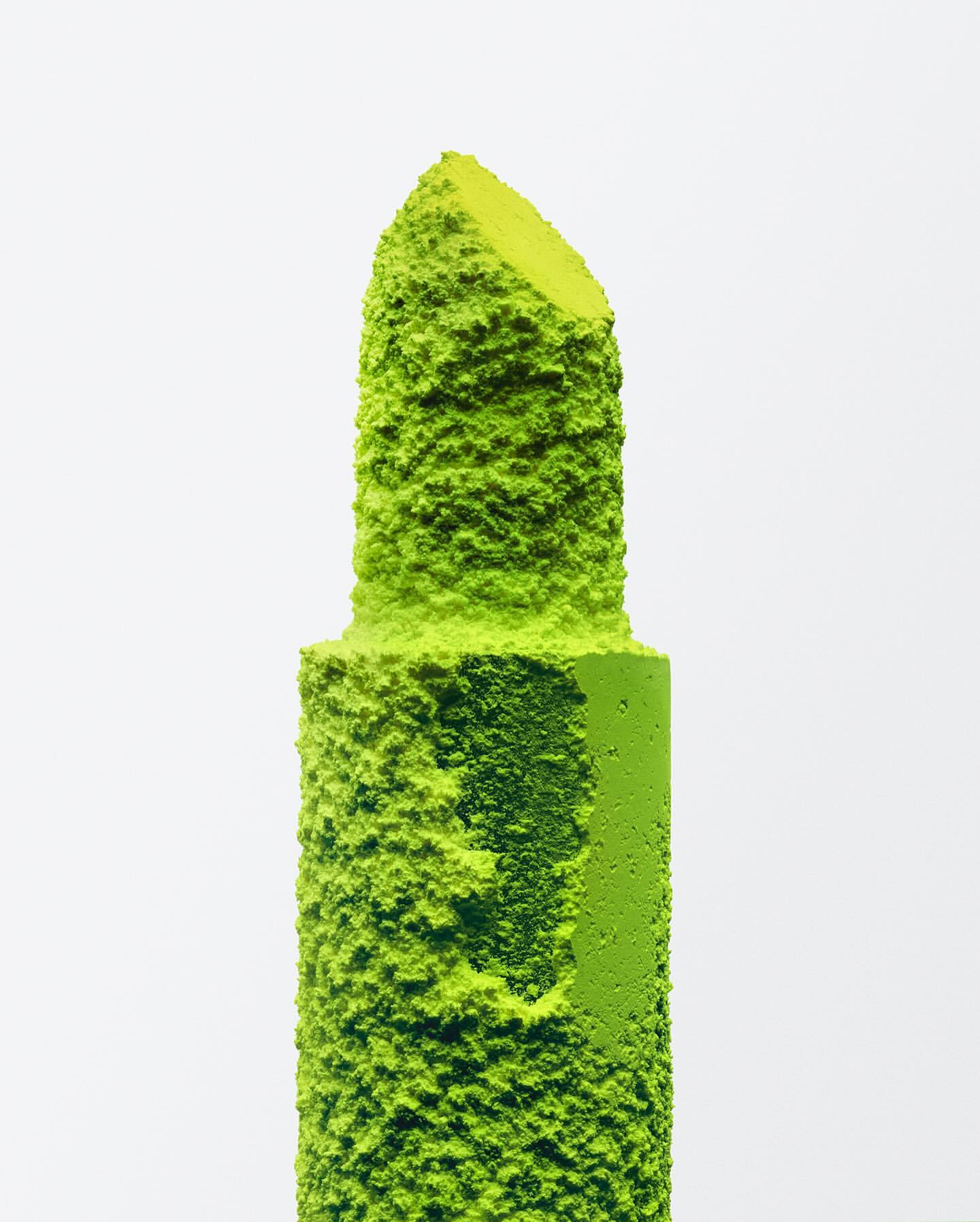 Close-up studio shot of neon green lipstick, coated with green powder on a white background. Beauty product, make-up, bold, unique.