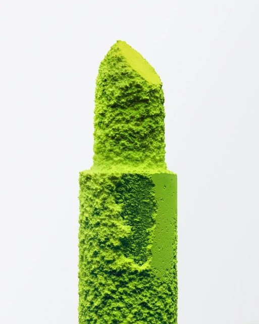 Close-up studio shot of neon green lipstick, coated with green powder on a white background. Beauty product, make-up, bold, unique.