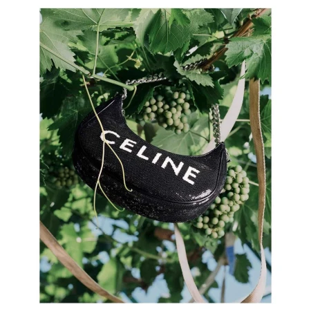 Celine handbag featuring the brand's logo against a background of green grape vines and leaves in an outdoor fashion setting.