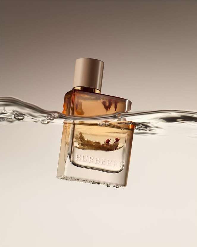 Burberry perfume bottle with tan liquid inside partially submerged in clear water against a gradient tan to off-white background.