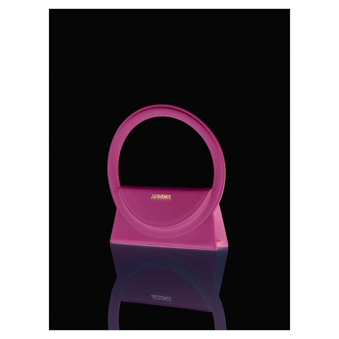 Stylish pink handbag with a unique circular handle and reflective surface against a dark backdrop. Fashion accessory.