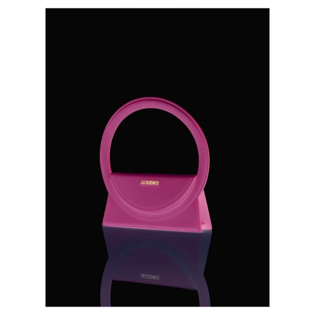 Stylish pink handbag with a unique circular handle and reflective surface against a dark backdrop. Fashion accessory.