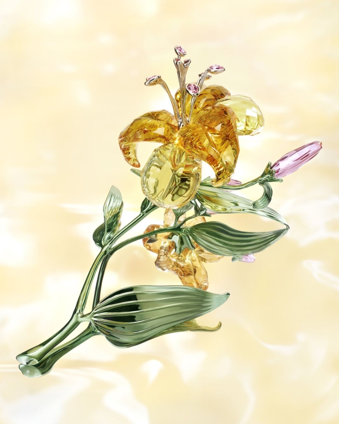 Crystal lily flower sculpture with yellow petals, green stem and leaves, and pink buds on a soft yellow background.