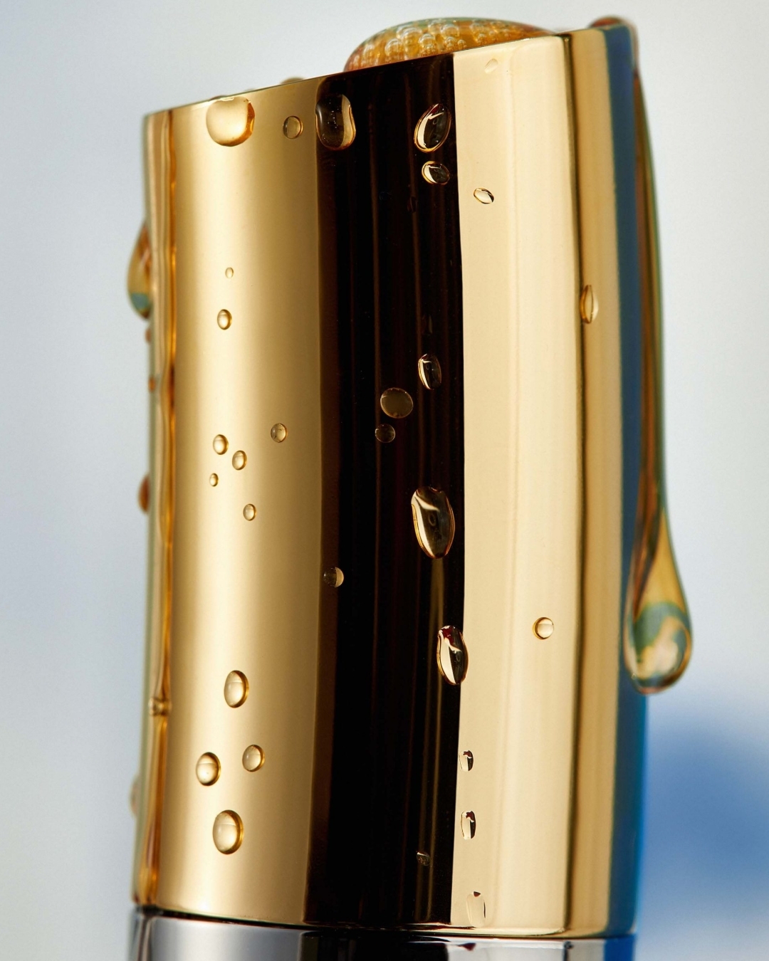 Close-up of a gold-colored perfume bottle cap adorned with water droplets, exuding a sense of luxury and quality against a soft backdrop.