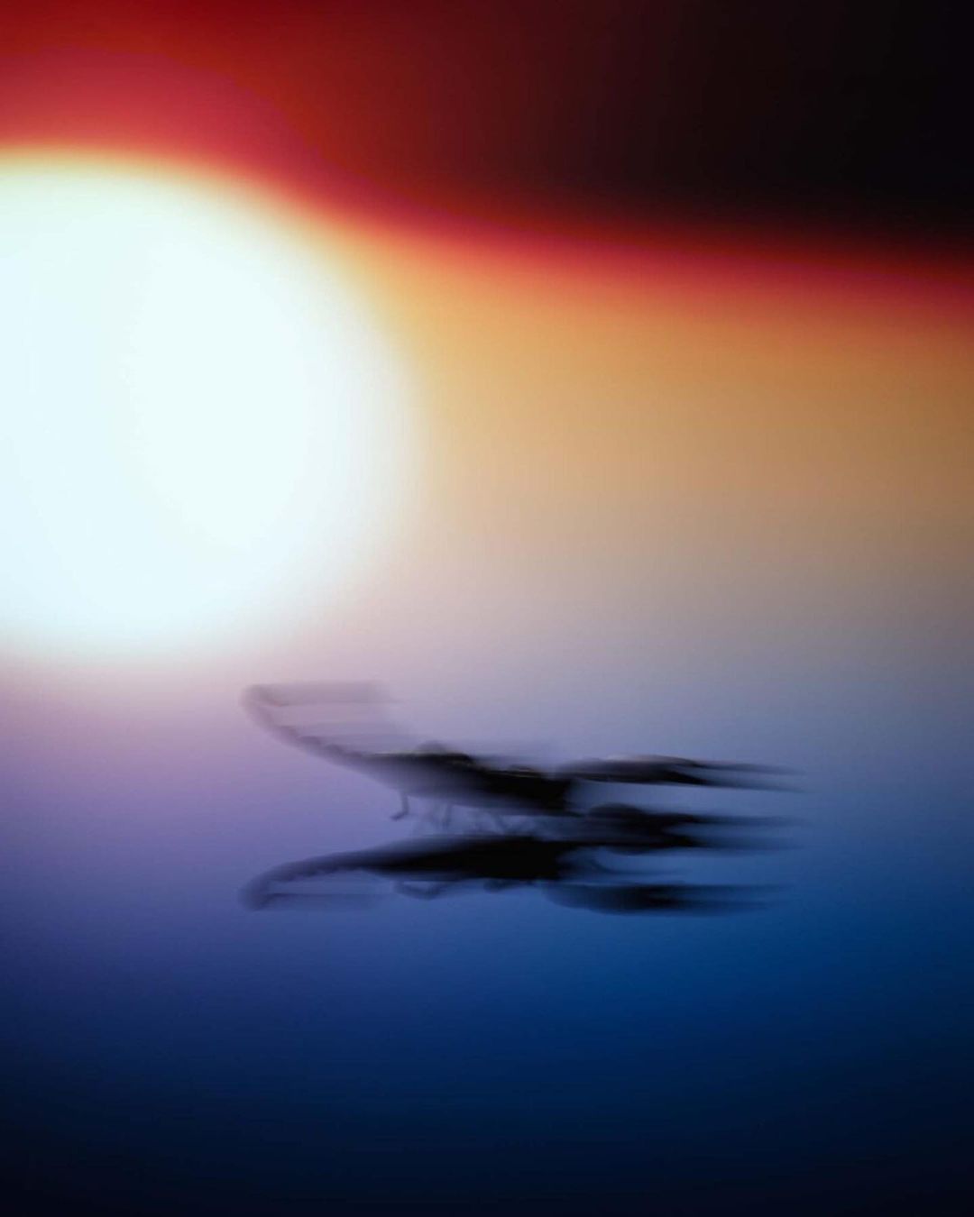 Abstract image of a blurred bird flying over water with a bright light source in the background, creating a sense of movement and light.