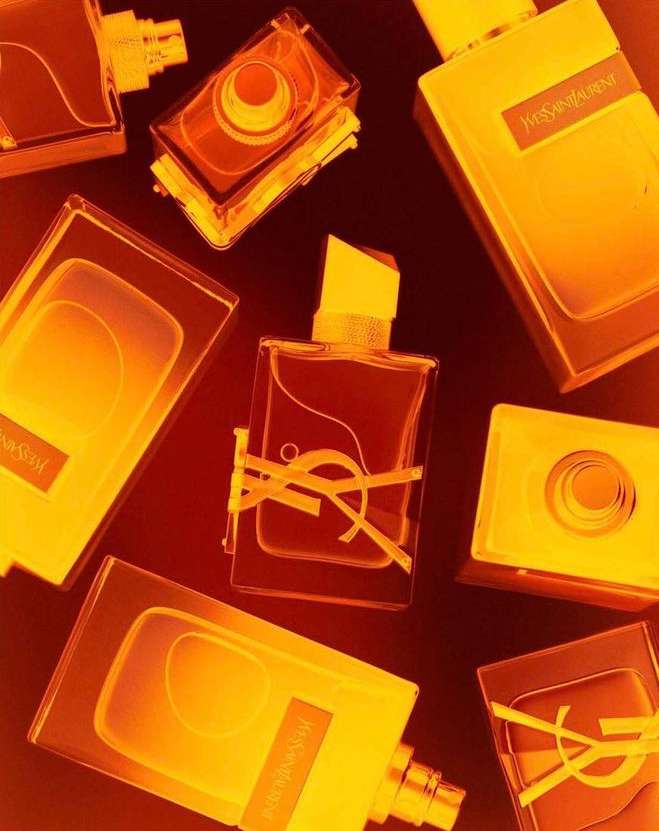 Several bottles of Yves Saint Laurent perfume are arranged on a dark surface, brightly lit with a warm, golden glow.