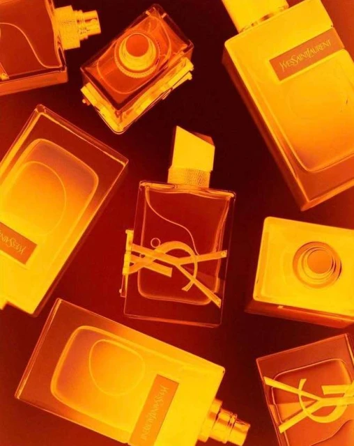 Several bottles of Yves Saint Laurent perfume are arranged on a dark surface, brightly lit with a warm, golden glow.