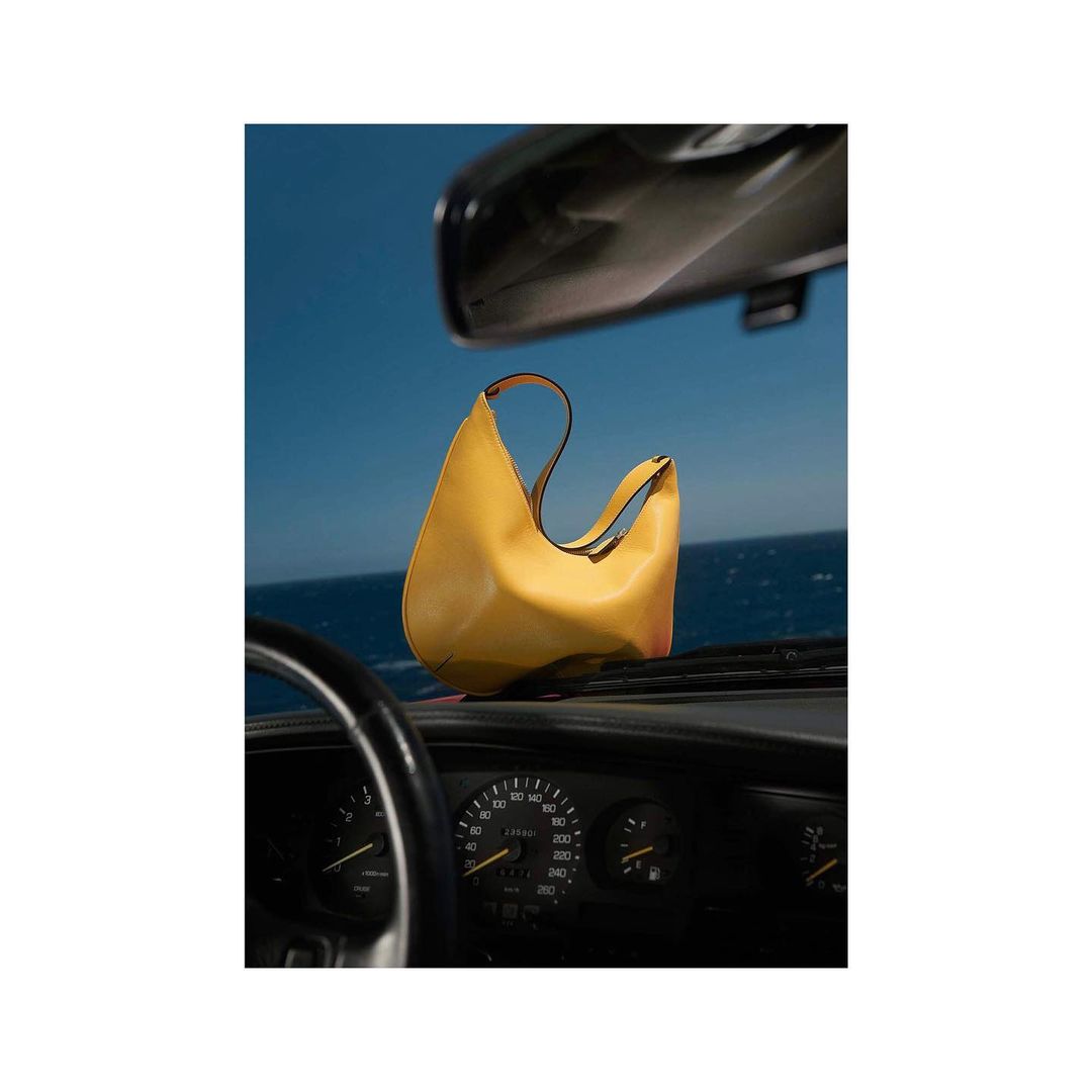 Yellow leather purse on a car dashboard against a blue ocean and sky. Fashion shot of an accessory with a travel backdrop.