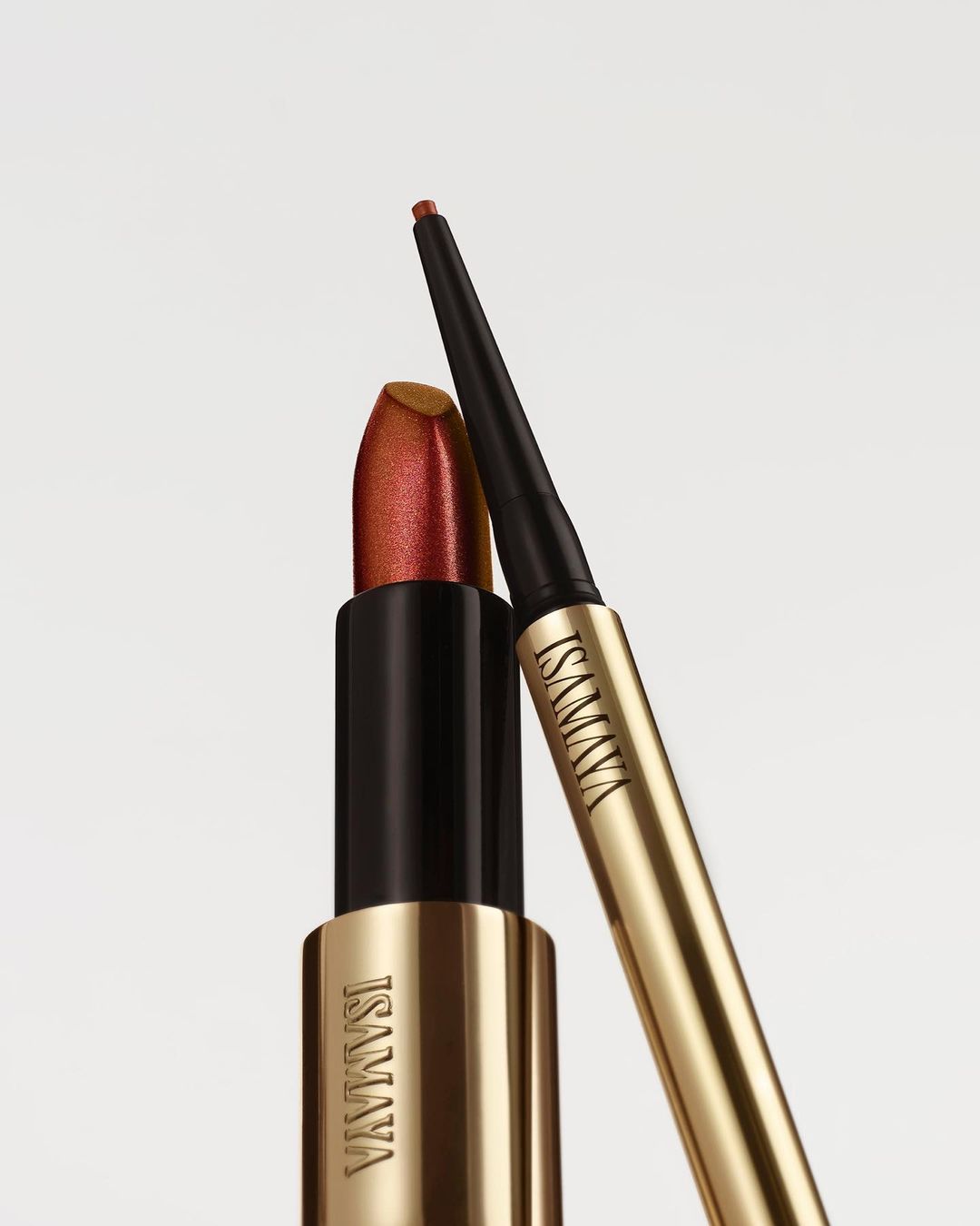 Still life shot of gold lipstick and black and gold eyeliner by ISAMAYA, against a white background, product shot for beauty.
