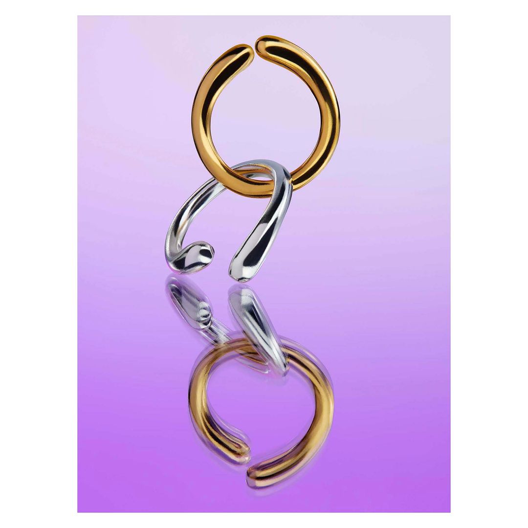 Interlocking gold and silver metal rings jewelry product shot against a purple background and reflective surface. Product photography.