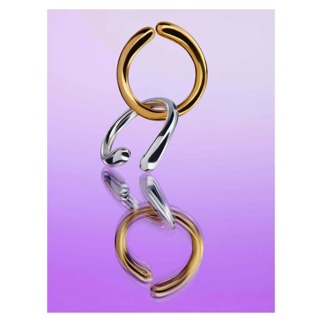 Interlocking gold and silver metal rings jewelry product shot against a purple background and reflective surface. Product photography.