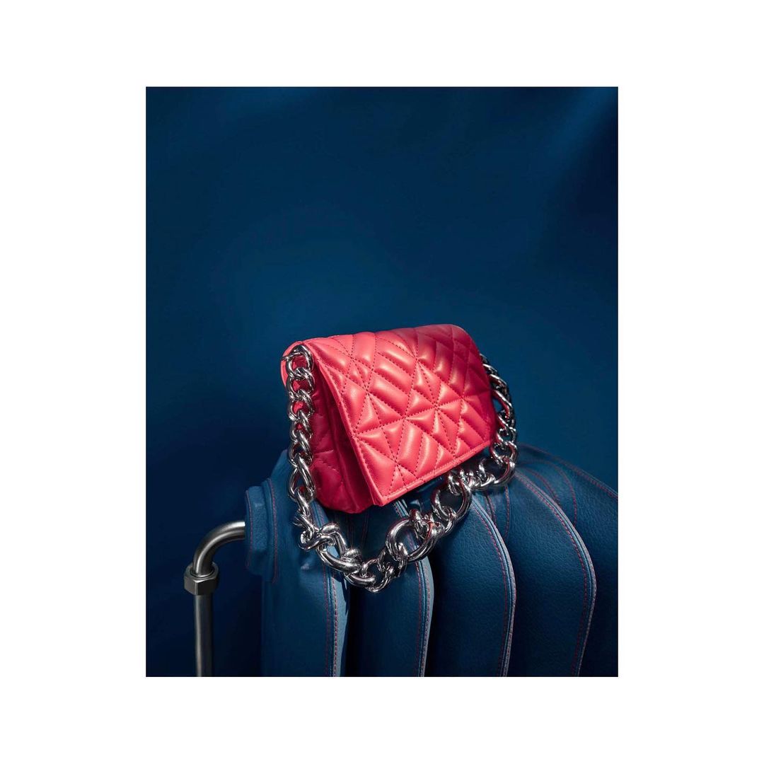 Red quilted bag with a chunky silver chain handle displayed against a dark blue background, positioned on a matching blue radiator.
