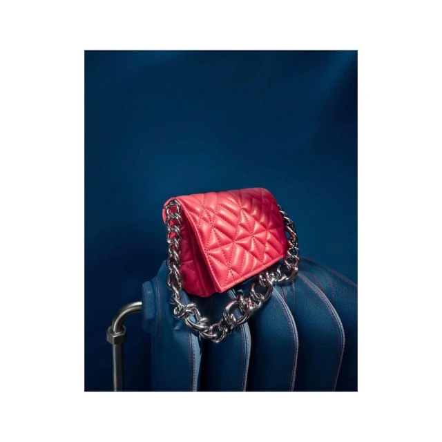 Red quilted bag with a chunky silver chain handle displayed against a dark blue background, positioned on a matching blue radiator.