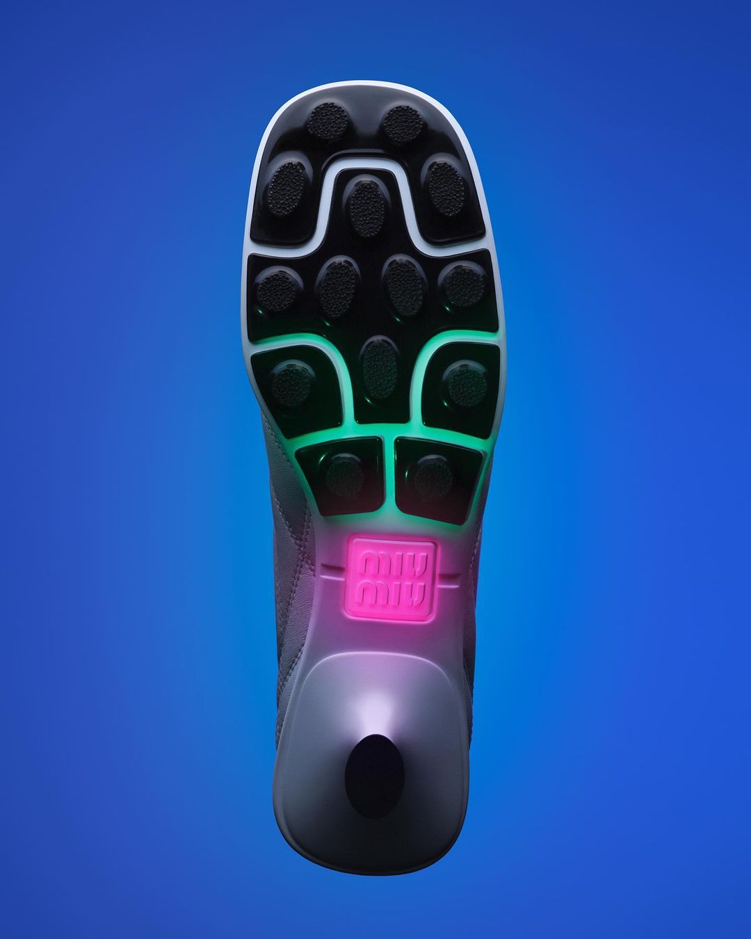 Elevated view of a single gray, black, white, green, and pink sport shoe on a blue background showcases its patterned sole design.