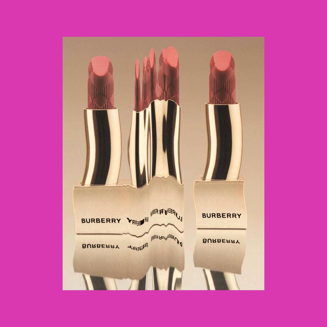 Three Burberry lipsticks are displayed, with a distorted reflection of one, set against a light gradient background and a pink square.