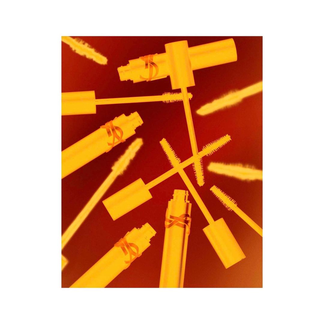 Close-up of yellow mascara tubes with wands on a red background. Cosmetic product shot for beauty, fashion, or promotional use.