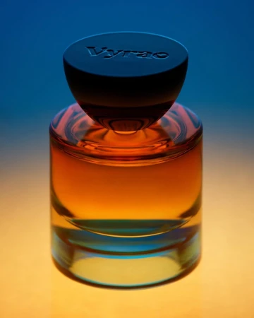 Amber glass perfume bottle with a dark rounded cap featuring embossed lettering against a blue and gold gradient background.