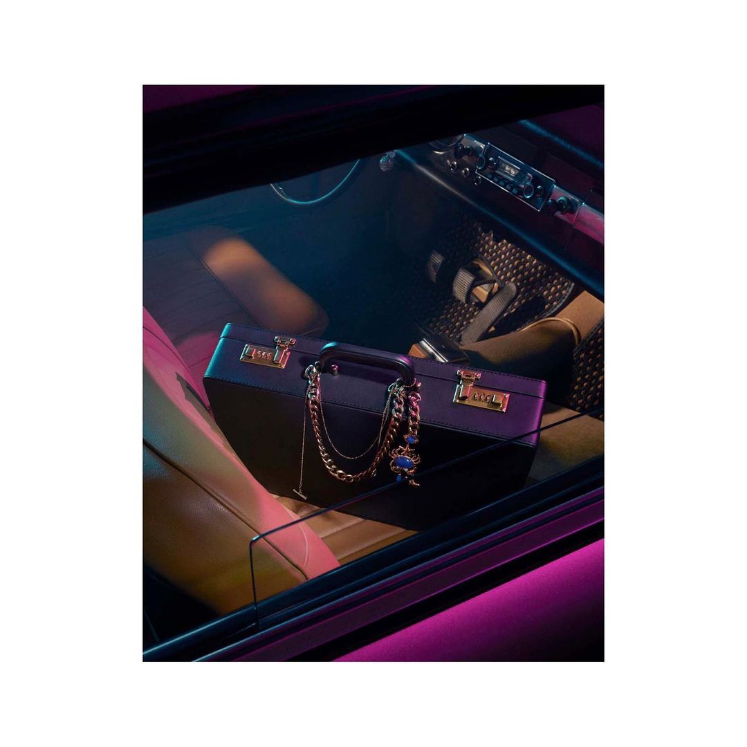 View of a dark blue briefcase with a gold chain inside of a car with pink interior lighting, creating a vibrant and stylish scene.