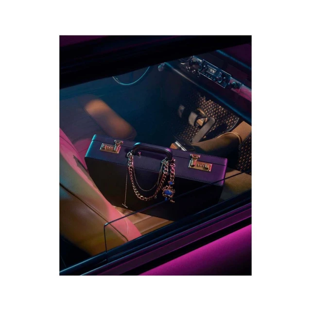View of a dark blue briefcase with a gold chain inside of a car with pink interior lighting, creating a vibrant and stylish scene.
