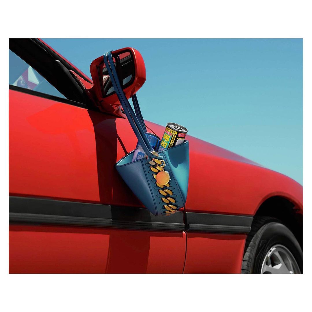 Red car exterior featuring a blue purse with gold chain detail hanging on the side mirror against a clear blue sky backdrop.