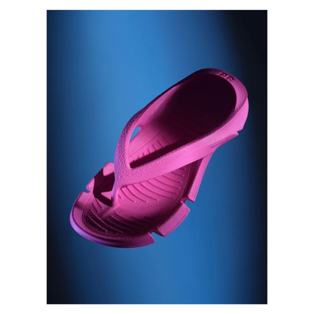 Close-up of a pink rubber flip-flop levitating in front of a blue gradient backdrop, showcasing product and sandal design details.