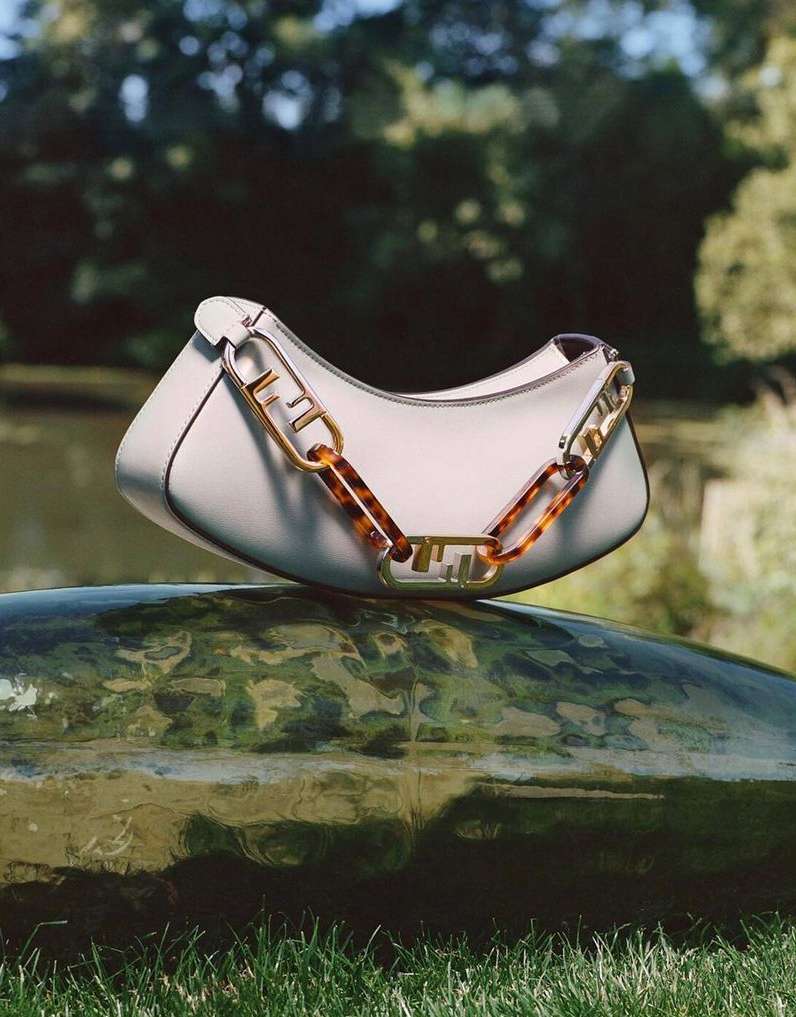 White Fendi handbag with a thick chain handle displayed on a wet rock in an outdoor nature setting with a blurred background.