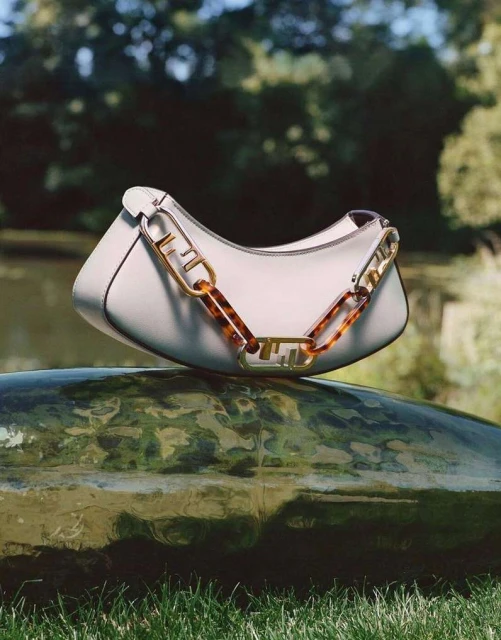 White Fendi handbag with a thick chain handle displayed on a wet rock in an outdoor nature setting with a blurred background.