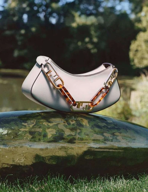 Fendi First Small handbag in white nappa leather with a metal F clasp and tortoise-shell-effect details. Outdoor setting on textured stone.