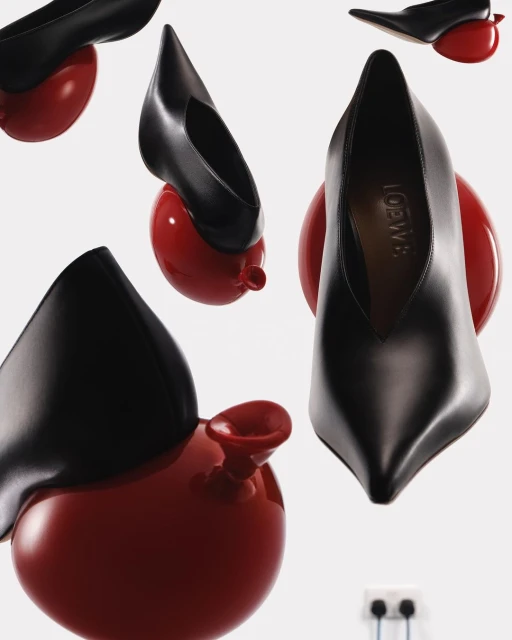 Still life of black leather high heel shoes on red balloon shaped heels in a pattern with white wall and electrical outlet background.