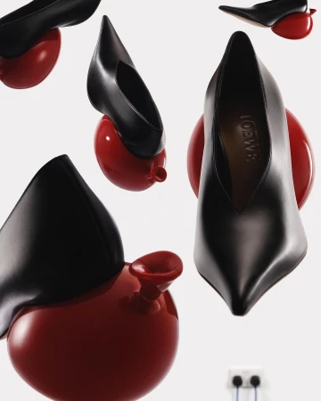Still life of black leather high heel shoes on red balloon shaped heels in a pattern with white wall and electrical outlet background.