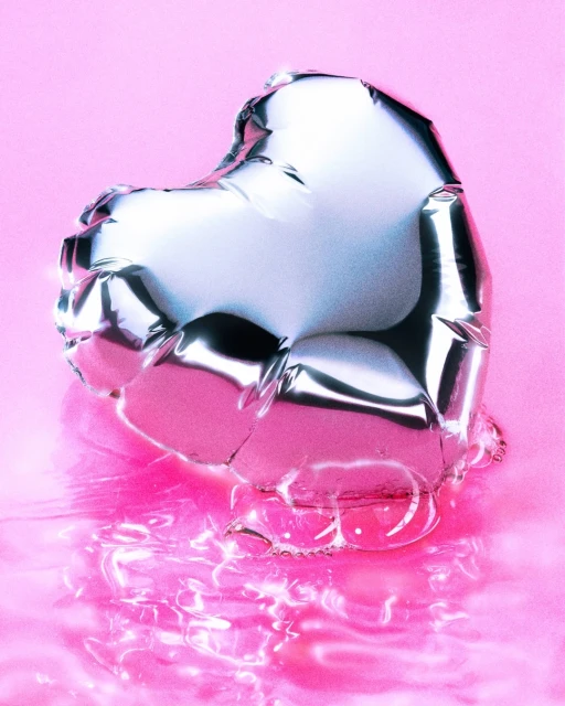 Silver heart-shaped balloon floating on a pink reflective surface. The balloon reflects the surrounding light and colors with a metallic sheen.