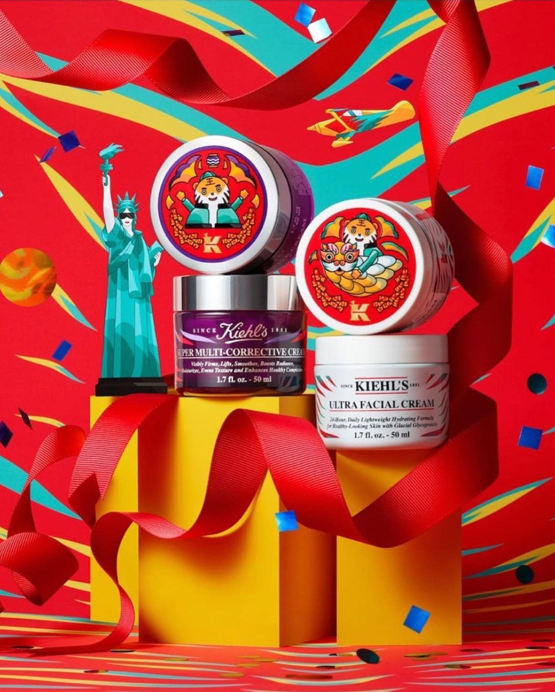 Kiehl's skincare products, including creams and serums, are displayed alongside a Statue of Liberty replica and red ribbons on yellow blocks.