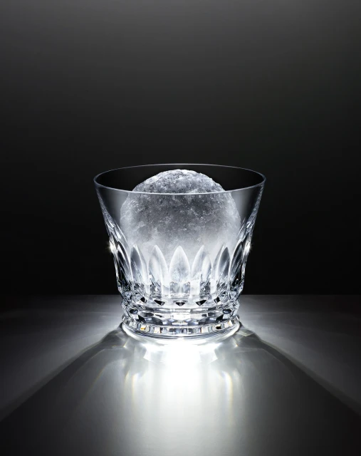 Crystal glass with faceted design, filled with crushed ice, against a dark backdrop and illuminated from below, casting shadows.